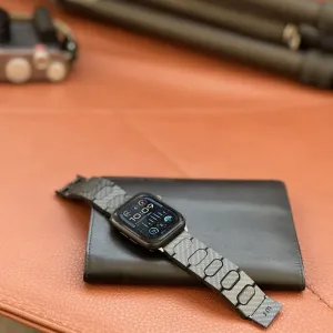 Just Mobile Apple Watch Armband aus Carbonfaser mit Magnetverschluss, gezeigt an einer Smartwatch auf einem Lederetui