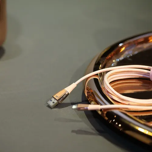 Lightning-kabel i roséguld med flätad sladd, USB-A till Lightning, delvis upprullad på bord bredvid blank oval metallbricka.