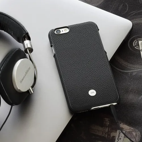 Black leather patterned iPhone case with openings for camera, buttons and ports; attached charging cable, phone on a laptop.