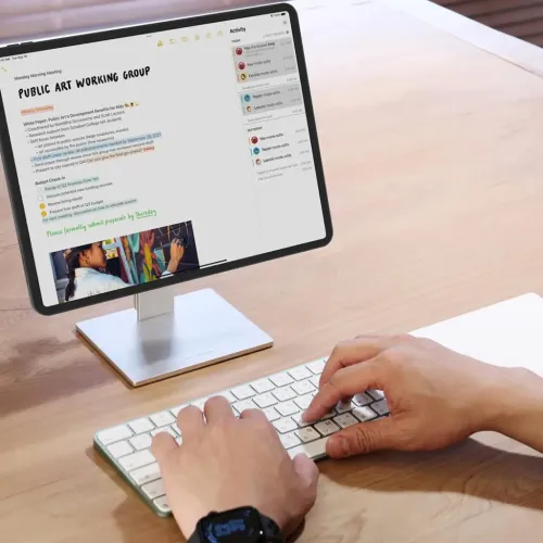 Silberner Tablet-Ständer aus Aluminium mit quadratischem Sockel und gerader Säule hält ein Tablet im Querformat auf einem Holzschreibtisch.