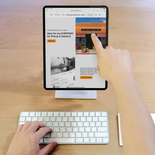 Tablet-Ständer aus silberfarbenem Aluminium mit flachem Fuß und schmaler Säule hält das Tablet aufrecht vor der Tastatur auf dem Schreibtisch.