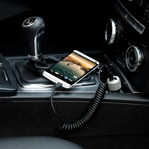 Dubbel USB-billaddare med två USB-A-portar i cigarettuttaget; spiralformad micro-USB-kabel till telefon på mittkonsol fram.