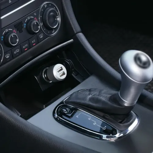 Dubbel USB-billaddare med två USB-portar i bilens cigarettuttag, synlig i mittkonsolen bredvid växelspak och reglage fram.