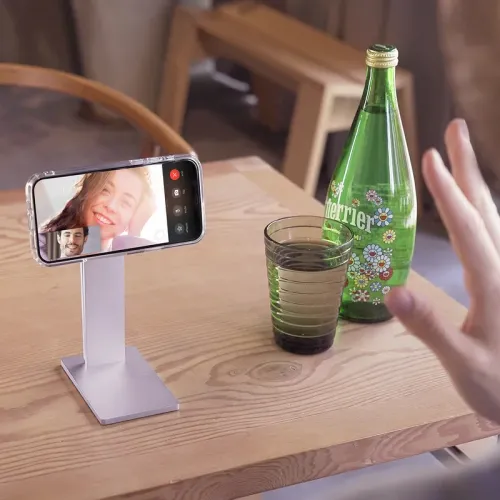 aluminum iPhone stand with rectangular base and pillars holds phone horizontally on table; glass and green bottle next to it.