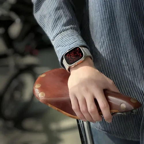 Titanium bracelet for Apple Watch Ultra in gray metal with link design, shown on wrist while hand holds a brown bicycle seat.