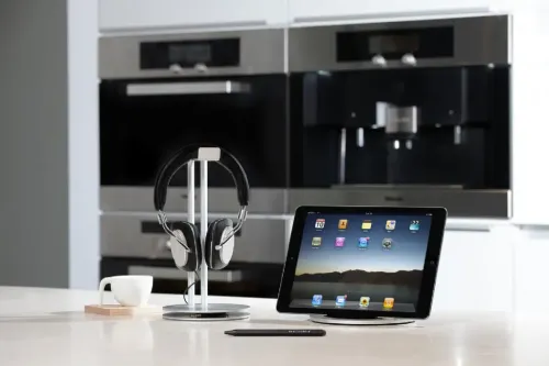 iPad-ställ i aluminium med rund bas håller iPad i liggande läge på köksbänk; låg profil, svart arm skymtar bakom på basen.
