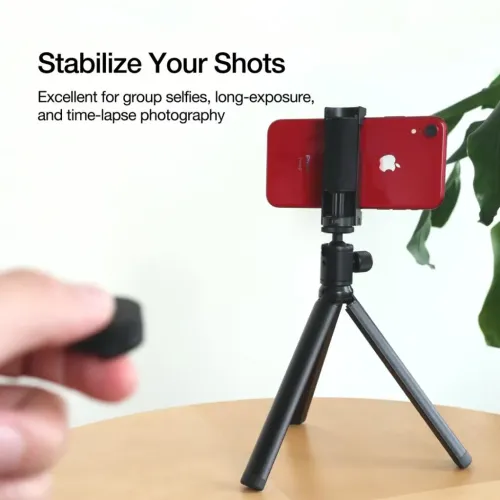 Just Mobile ShutterGrip Tripod med treben och kulled håller röd smartphone liggande i klämma på ett bord; fjärr i förgrund.