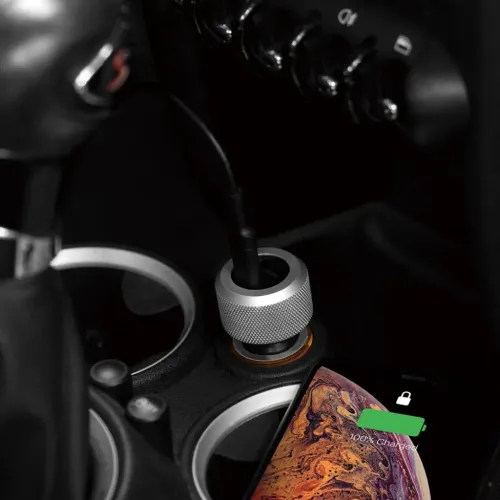 Just Mobile Highway Max billader i riflet aluminium, plugges inn i bilens 12 V-uttak med kabelen satt inn; telefonen lades ved siden av.